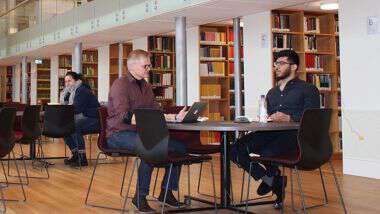 Bilde av to personer som sitter ved et bord i et bibliotek