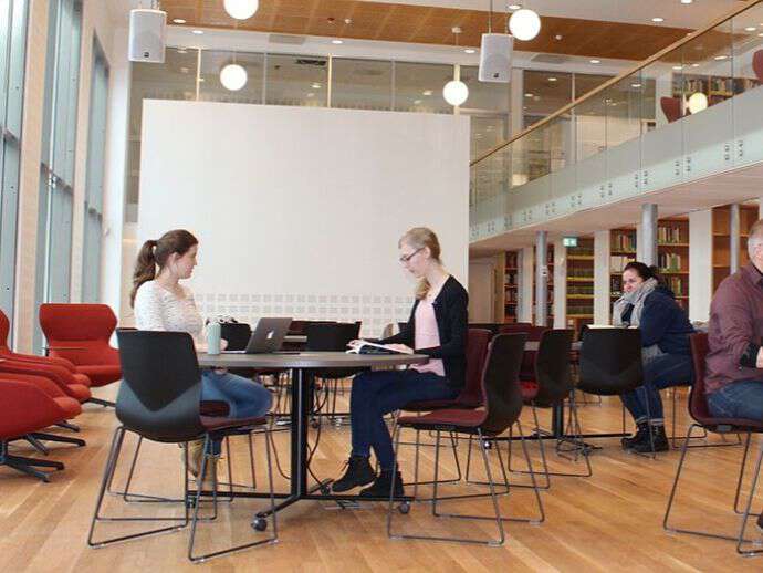 Tre personer som sitter ved bord i et bibliotek