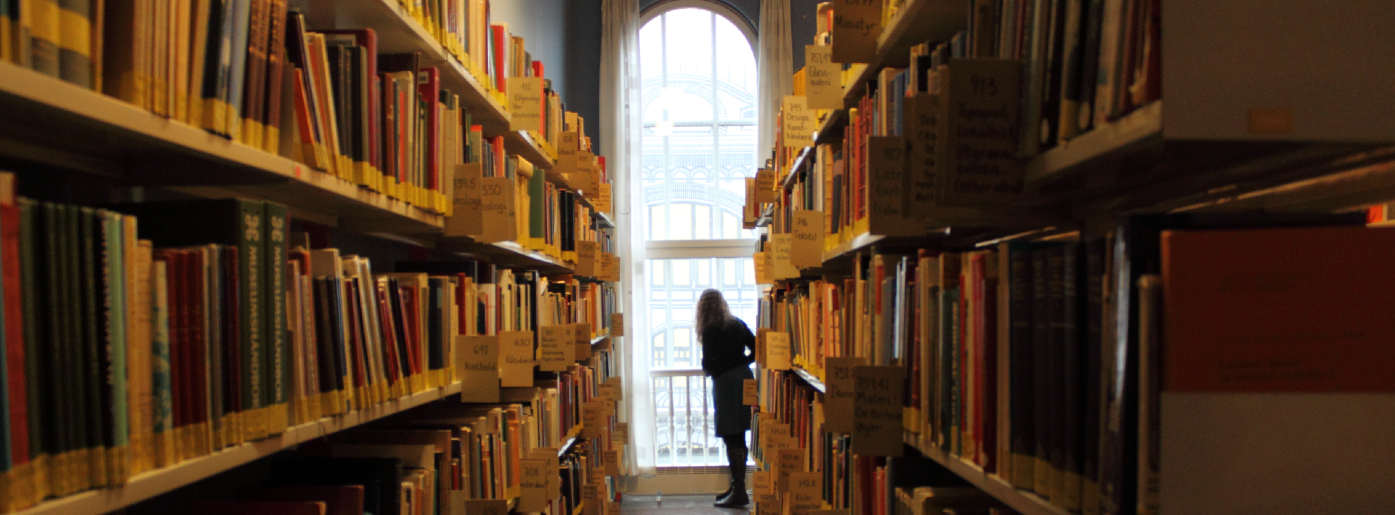 Book shelve, and a woman looking out the window at the end of the room