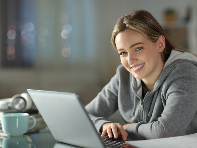 Bilde av en smilende student som jobber på en datamaskin.
