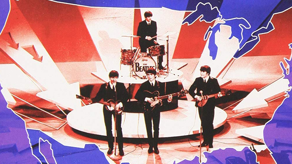 Picture of the band The Beatles. Four young men playing instruments with the US flag in the background.