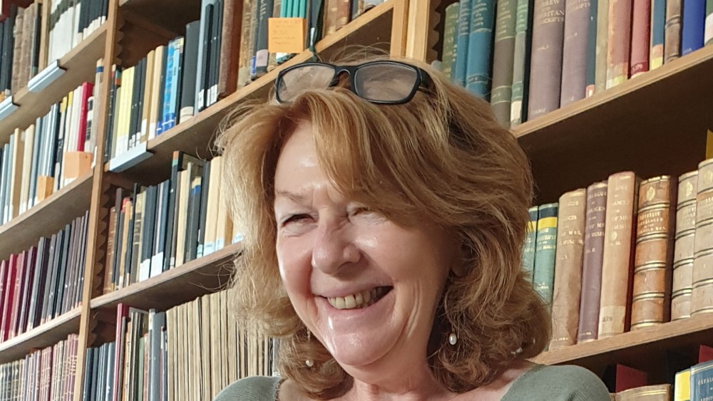 Photo of Prof. Dr. Ira Rabin standing in front of a bookshelf, smiling with glasses on her head.
