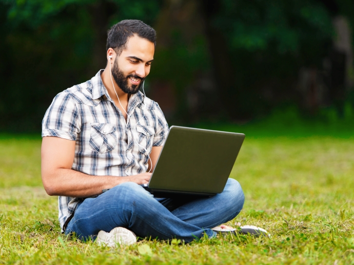 Mann med laptop som sitter på gresset.