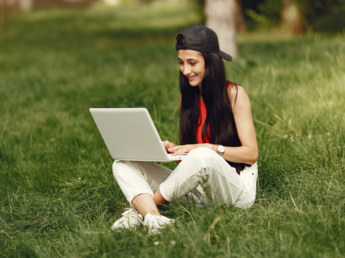 Foto av student som sitter i gresset med laptop.