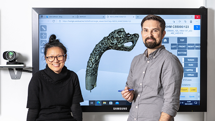 Photo of two smiling people standing in from of a digital screen.
