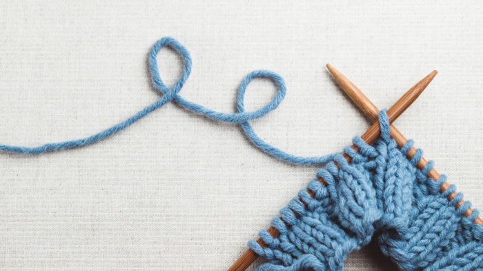 Blått garn og strikkepinner med påbegynt strikketøy