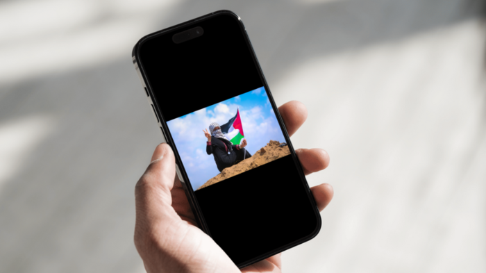 Hånd som holder en mobil der det vises et bilde av en kvinne som holder palestinsk flagg.
