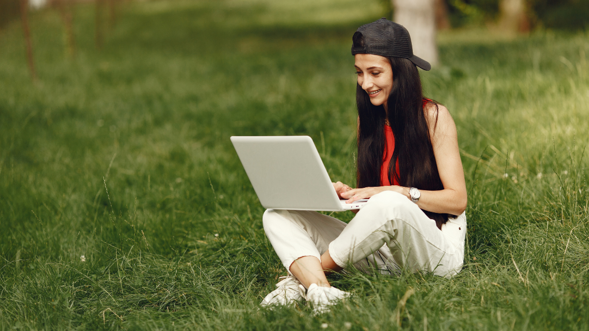 Foto av student som sitter på gresset med laptop i fanget.