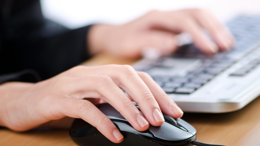 Photo of hands on a computer mouse and keyboard.